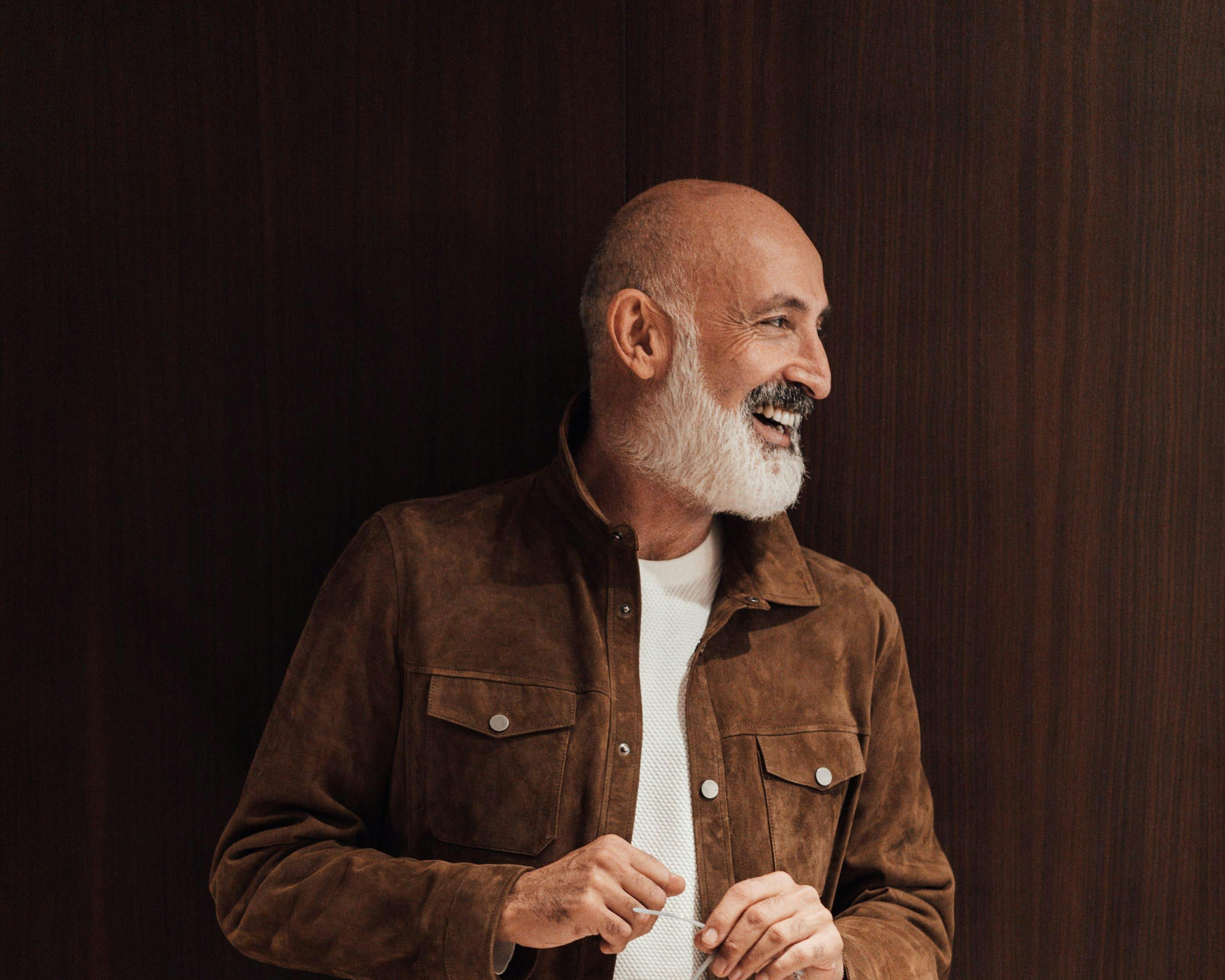Man wearing a brown jacket over a white shirt against a dark background